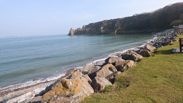 Un paysage côtier caractérisé par une côte rocheuse, une zone herbeuse et une vue sur la mer.