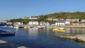 A harbor with boats docked, buildings on a hillside, and a clear sky. - Kernyk (Helston)