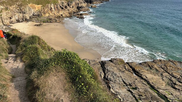 A coastal landscape with a rocky cliff, a sandy beach, and a clear view of the ocean. - Kernyk (Helston)