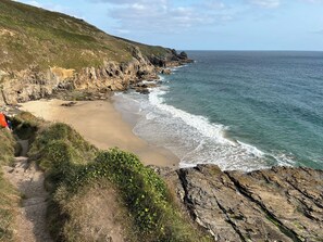 A coastal landscape with a rocky cliff, a sandy beach, and a clear view of the ocean.