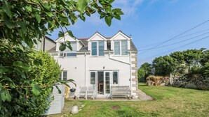 A two-story house with a white exterior, a front porch with a bench, and a small garden area. - Kernyk (Helston)