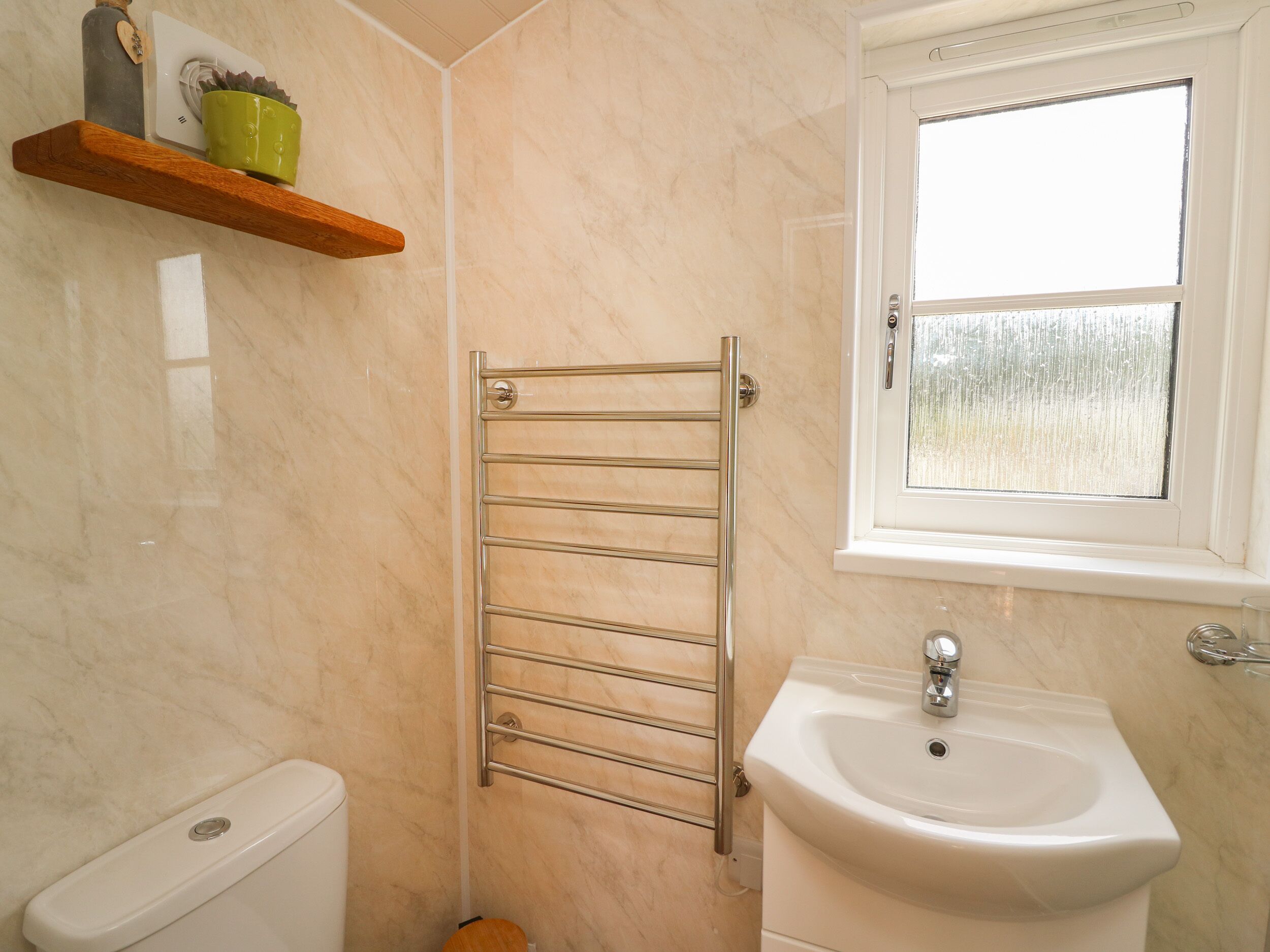 A bathroom with a toilet, a sink, a towel rack, and a window.