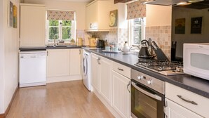 A modern kitchen with white cabinetry, a built-in oven, a microwave, and a gas stove. There is a washing machine and a sink with a window above it. - Mimi's Cottage (Liskeard)