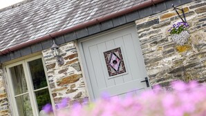 A stone building with a white door, a window, and a hanging flower basket. - Mimi's Cottage (Liskeard)