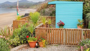Een kusttuin met houten omheining, een turquoise schuurtje en een vlag.