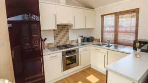 A compact kitchen with white cabinets, a built-in oven, a microwave, and a sink. - Jules @ 79 (Narberth)