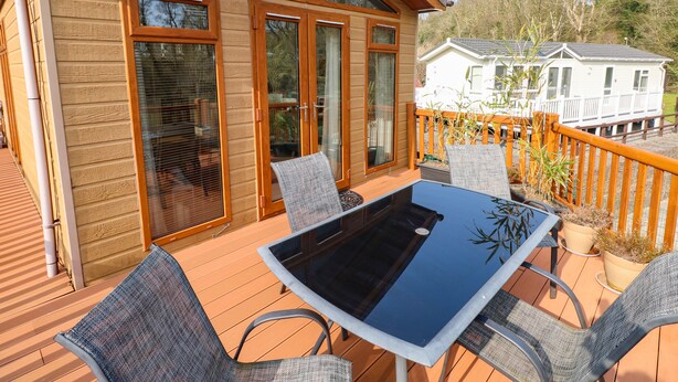 A wooden deck with a glass table and chairs, large windows, and a view of a white house in the background. - Jules @ 79 (Narberth)