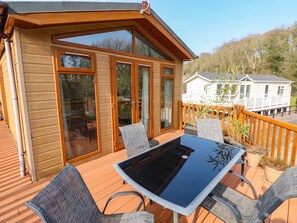 A wooden deck with a glass table and chairs, large windows, and a view of a white house in the background. - Jules @ 79 (Narberth)