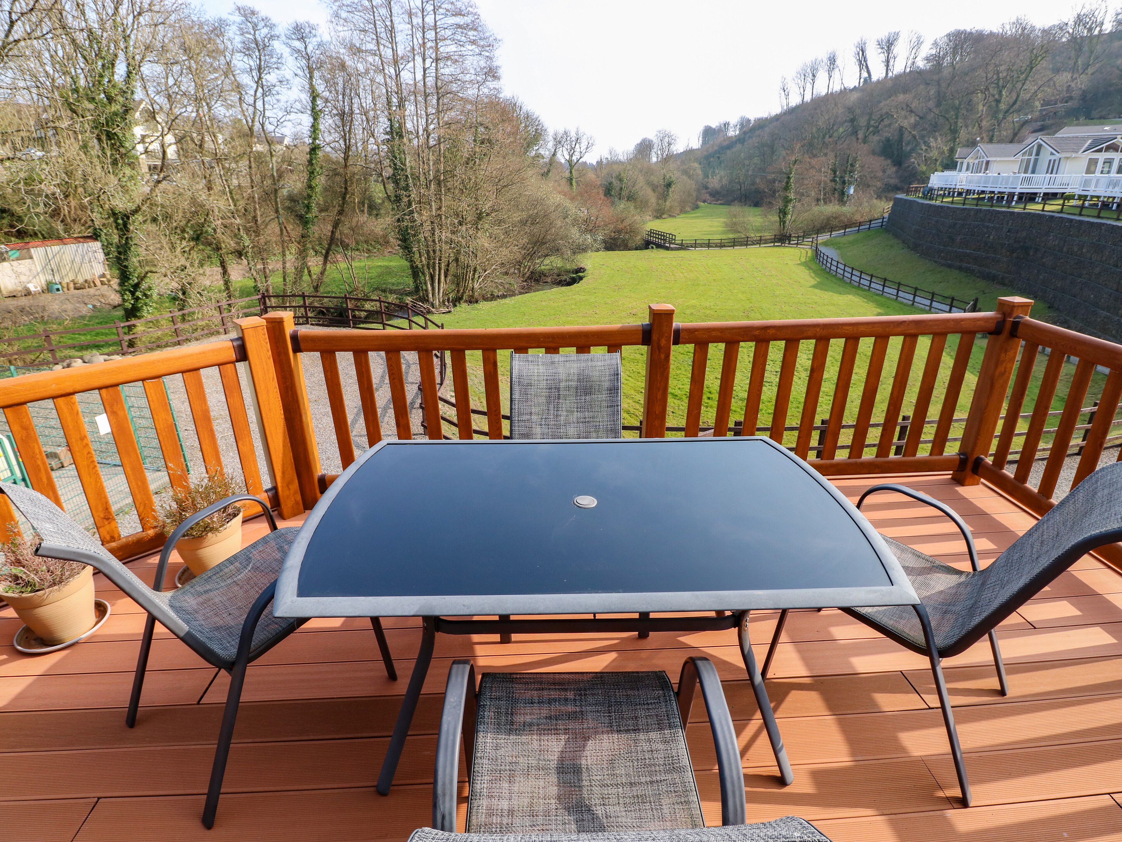 A deck with a table and chairs, overlooking a green landscape with trees and a building in the distance.