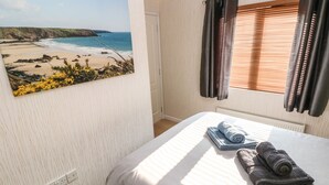 A bedroom with a beach view painting, a bed with rolled towels, and a window with blinds. - Jules @ 79 (Narberth)