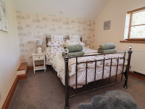 A bedroom with a bed, nightstand, and a window with blinds. - Ash Farm Cottage (Holywell)