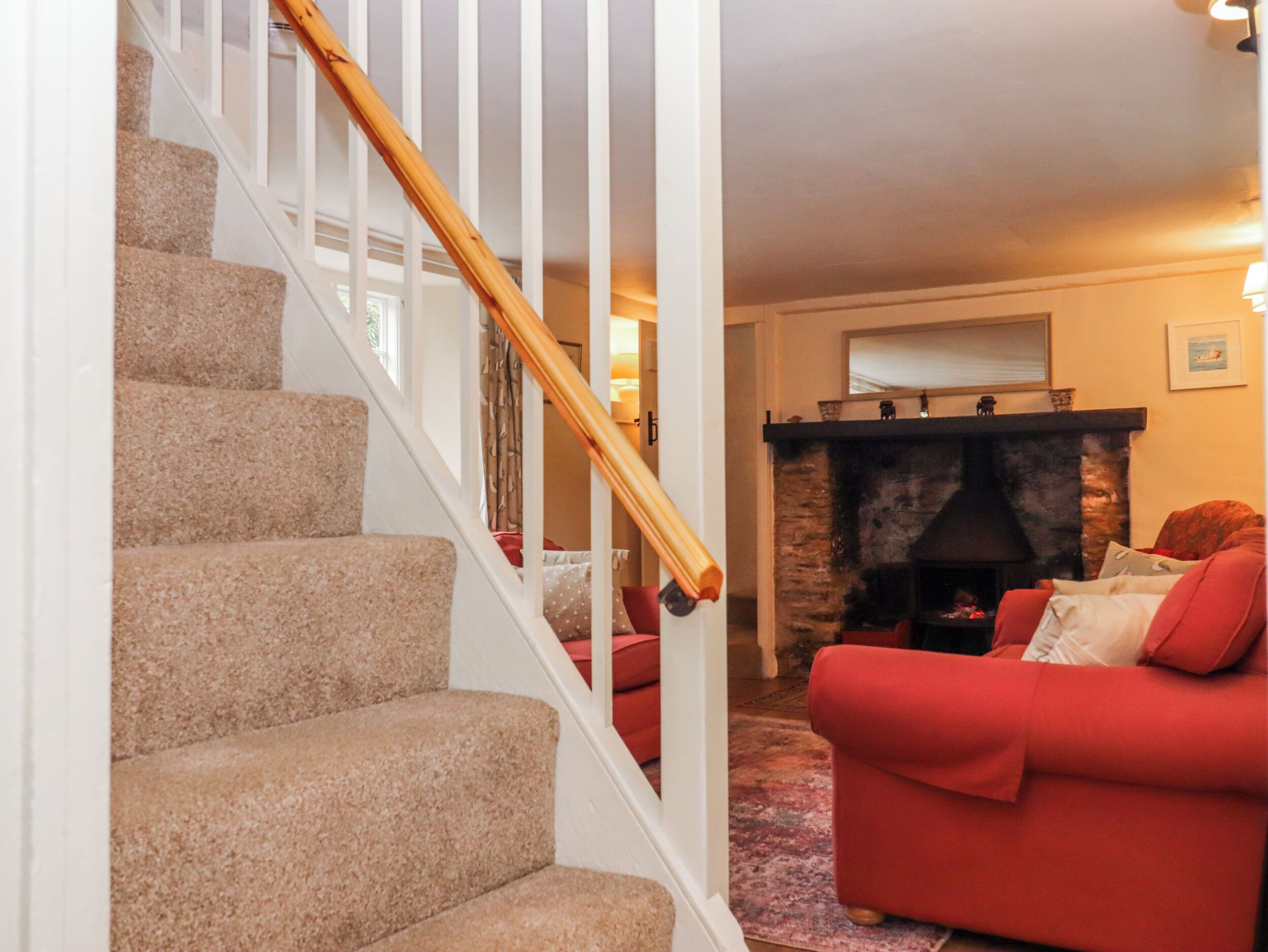 A staircase with carpeted steps and a wooden handrail, leading to a living room with a red sofa and a stone fireplace.
