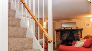 Un escalier avec des marches recouvertes de moquette et une rampe en bois, menant à un salon doté d’un canapé rouge et d’une cheminée en pierre.