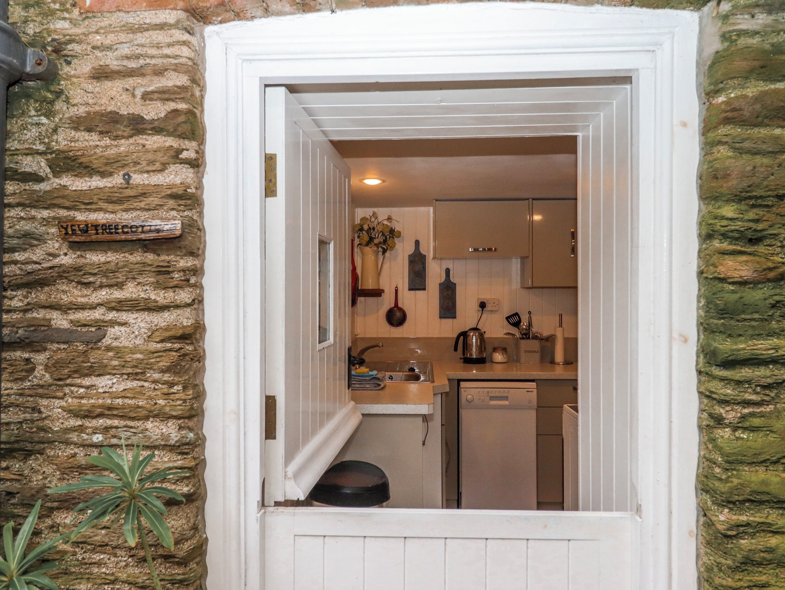 A narrow doorway leading into a compact kitchen with a dishwasher, a sink, and a countertop.
