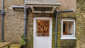 Un bâtiment en pierre avec une porte et une fenêtre blanches, un banc et des plantes en pot.