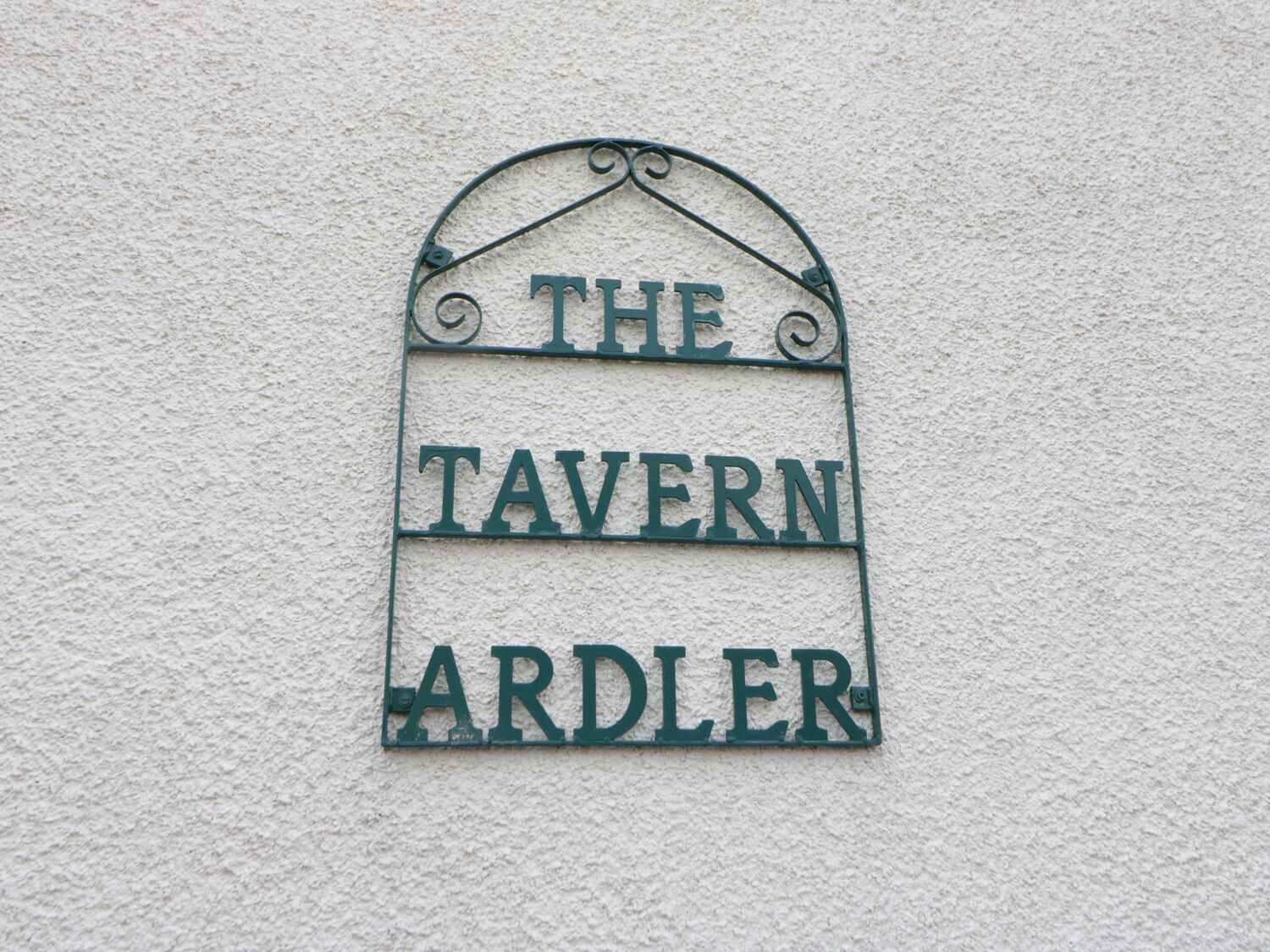 A sign with the words "THE TAVERN" and "ARDLER" on a textured wall.