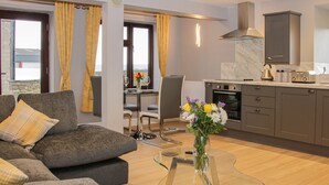 A modern living room with a grey sofa, a glass coffee table, and a dining area with a table and chairs. - Alders View Coach House (Craven Arms)