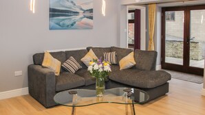 A modern living room with a grey sofa, a glass coffee table, and a vase of flowers. - Alders View Coach House (Craven Arms)