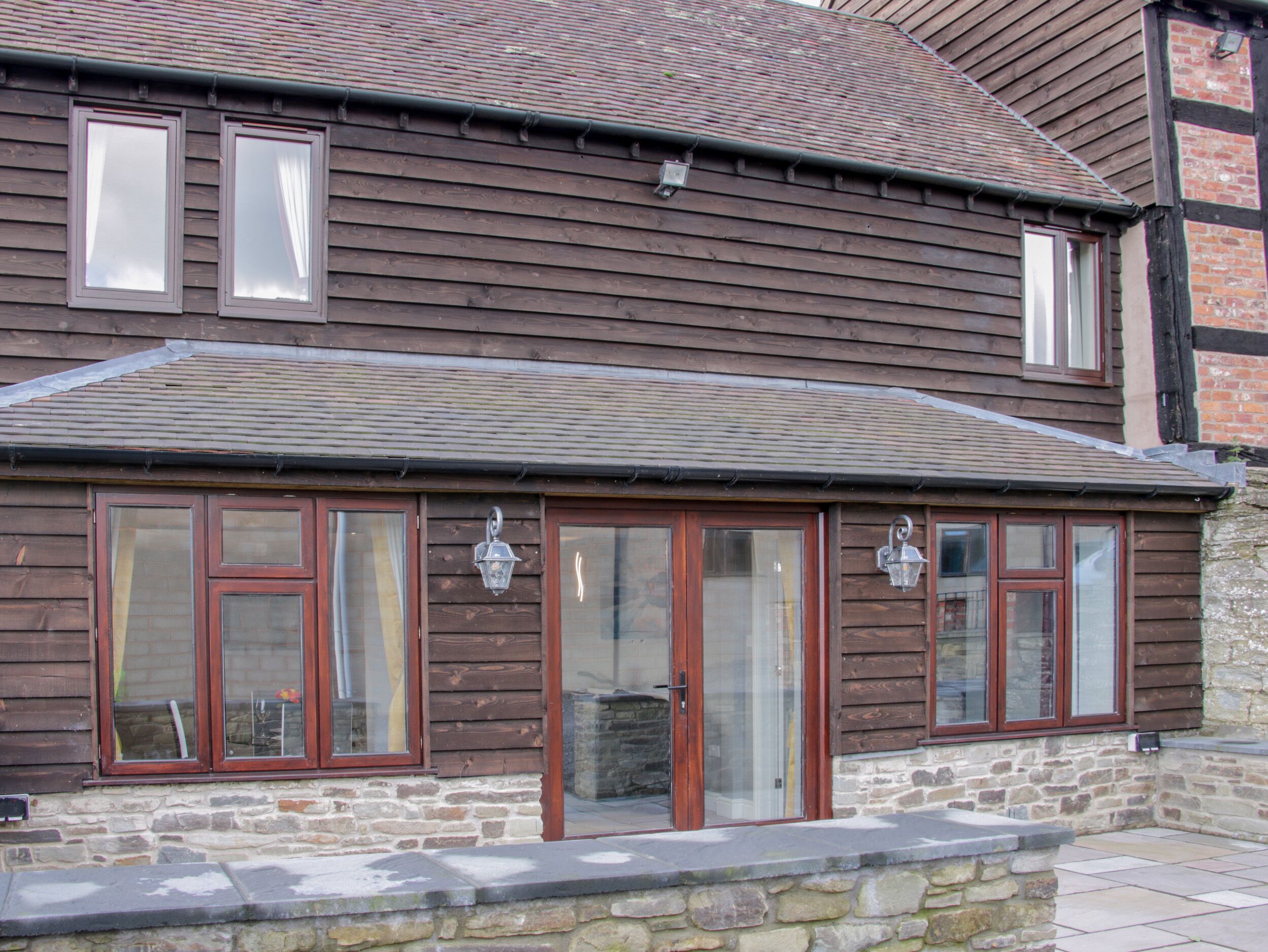 A two-story building with a stone foundation and wooden siding. It features large windows with wooden frames and a stone chimney.