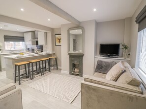 A modern kitchen with a central island, bar stools, a fireplace, and a television in a living area with a sofa and a patterned rug. - 5 Coley Lane (Stafford)