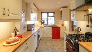 Une cuisine avec des meubles blancs, un lave-vaisselle rouge, une cuisinière et un four à micro-ondes.