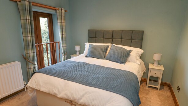 Une chambre avec un grand lit, une table de chevet, une fenêtre avec des rideaux et un radiateur.