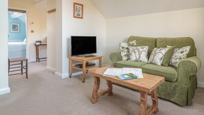 Ein Wohnzimmer mit einem grünen Sofa, einem Holztisch, einem Fernseher auf einem Holzständer und einem gerahmten Bild an der Wand.