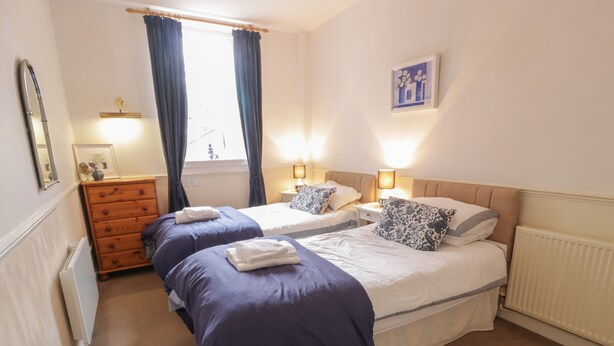 A hotel room with two beds, a dresser, a window with curtains, and a framed picture on the wall. - Turret Cottage (Prestonpans)