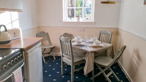 A small kitchen with a stove, a toaster, and a window with a view of trees. - Turret Cottage (Prestonpans)