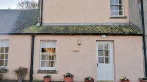 A two-story building with a white door and windows, a sign reading "Turret", and potted plants along the front. - Turret Cottage (Prestonpans)