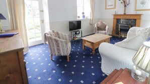 A living room with a fireplace, a television, and a patterned armchair. - Turret Cottage (Prestonpans)