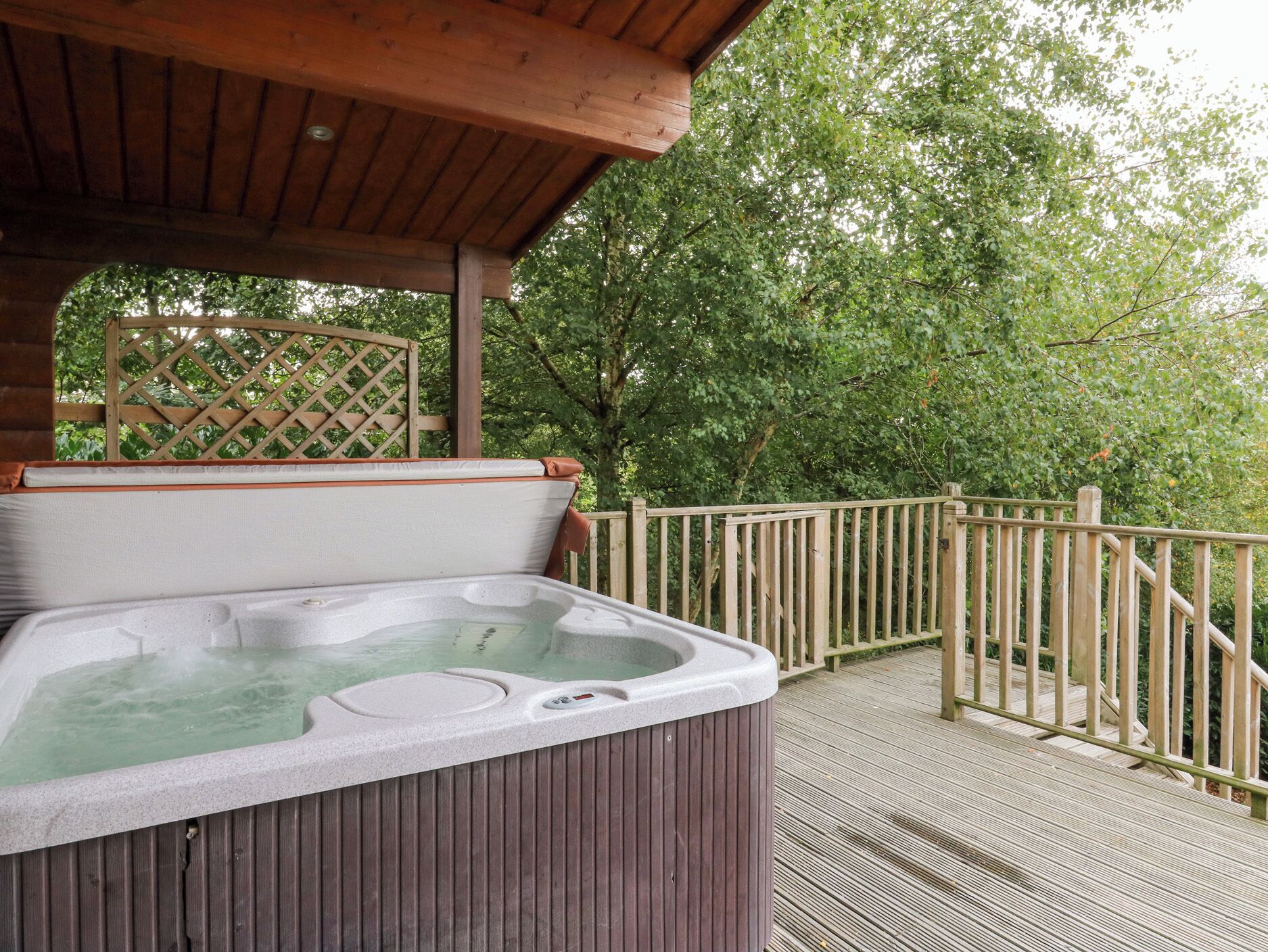 A hot tub on a wooden deck with a wooden fence and trees in the background.