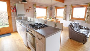 A kitchen with a central island, wooden cabinets, a stove, and a dining area with a table and chairs. - Barn Owl Lodge (Rhayader)