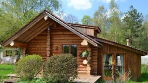 A rustic log cabin with a pitched roof, a front porch, and a small garden area. - Cozy Log Chalet with Terrace, Near Alsace and Ski Resorts (Le Saulcy)