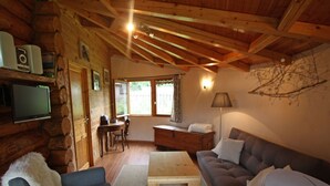 A cozy log cabin interior with a sofa, a table, a TV, and a lamp. - Cozy Log Chalet with Terrace, Near Alsace and Ski Resorts (Le Saulcy)