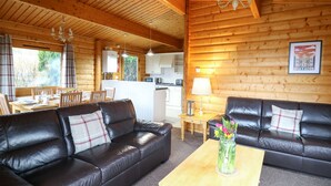A log cabin interior with a dining area, kitchen, and two leather sofas with cushions. - Valley View (Rhayader)