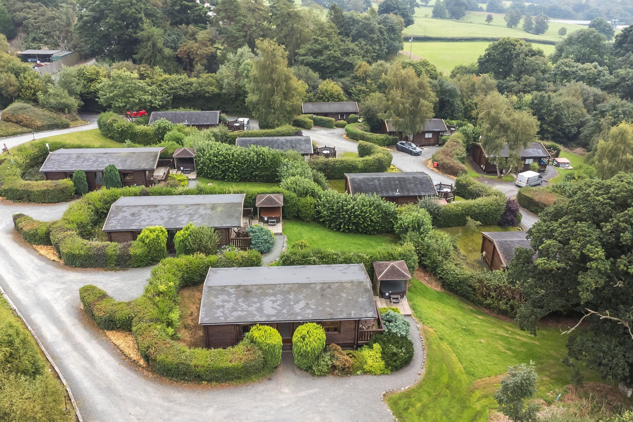 An aerial view of a residential area with multiple houses, each surrounded by well-maintained lawns and hedges.
