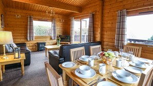 A wooden cabin interior with a dining area set for four, a sofa, and a television. - Valley View (Rhayader)