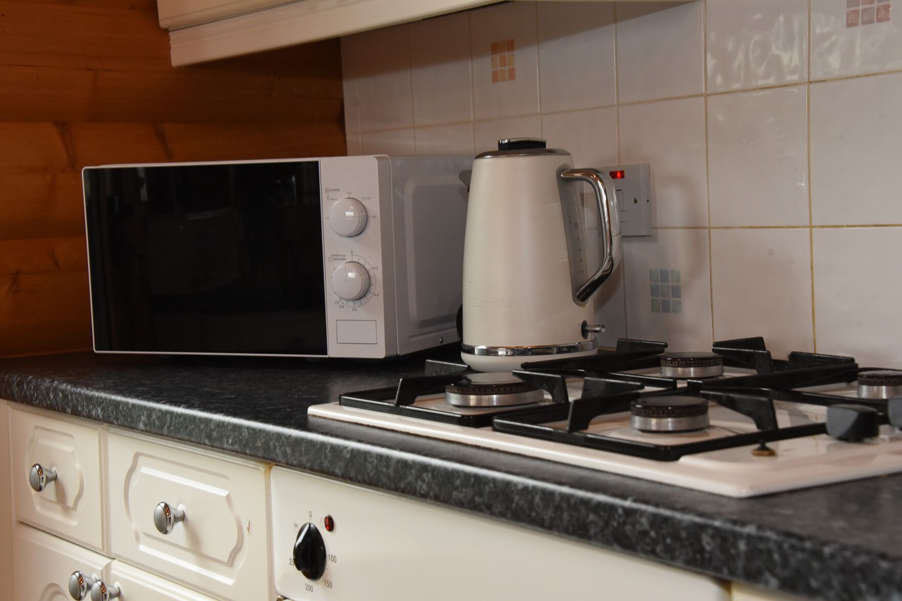 A kitchen with a microwave, a kettle, and a gas stove.