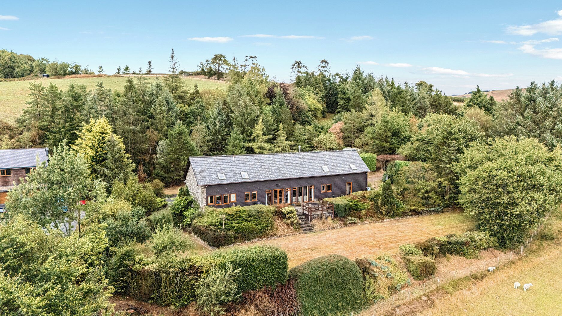 A stone building with a sloped roof surrounded by dense forest and rolling hills.