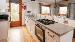 Een compacte keuken met een centraal eiland, houten balken, een witte koelkast en een raam met gordijnen.