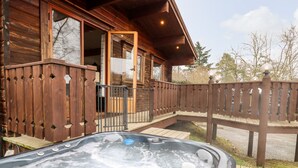 Een houten blokhut met een hottub op het terras, een houten omheining en een houten trap die naar de ingang leidt.