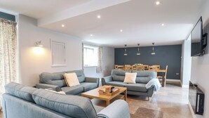 A modern living room with two grey sofas, a wooden coffee table, and a dining area with wooden chairs and a table. - Ysgubor Tyddyn Isaf (Corwen)