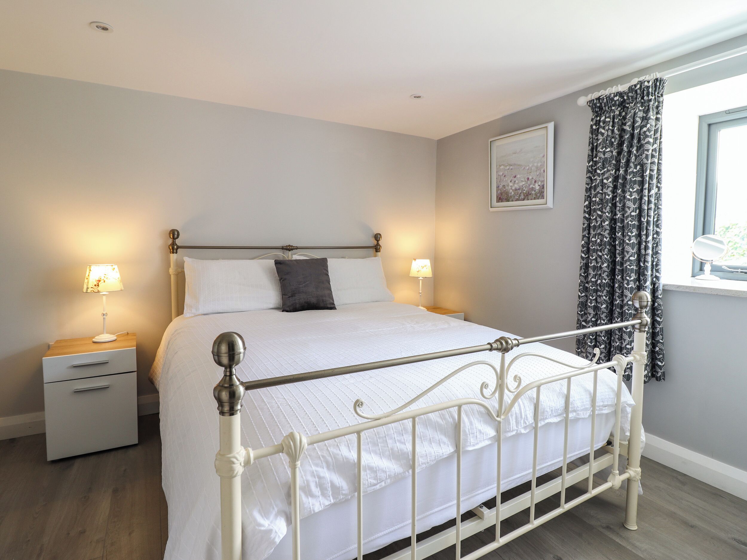 A neatly made bed with white bedding, a bedside table with a lamp, and a window with curtains.