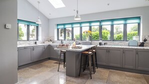 A modern kitchen with grey cabinets, a marble countertop, and a central island with stools. - Ysgubor Tyddyn Isaf (Corwen)
