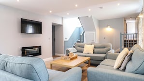 A modern living room with a flat-screen TV, grey sofas, a wooden coffee table, and a staircase leading to a balcony. - Ysgubor Tyddyn Isaf (Corwen)