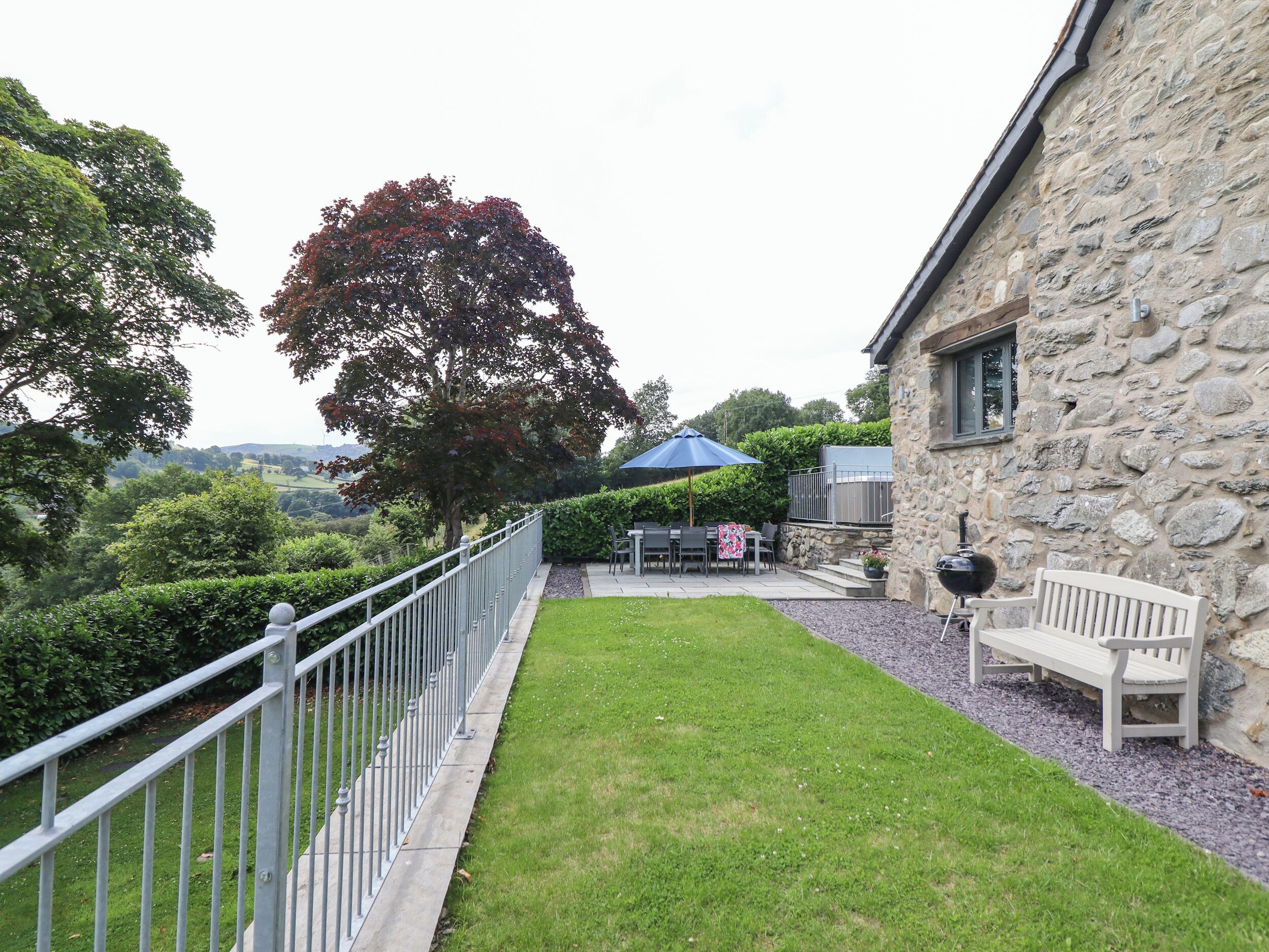 A stone building with a stone wall, a grassy lawn, a metal fence, a bench, and a table with chairs.