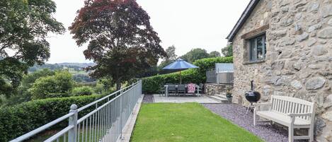 A stone building with a stone wall, a grassy lawn, a metal fence, a bench, and a table with chairs.