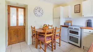 Uma cozinha com mesa de madeira, cadeiras, relógio e fogão.