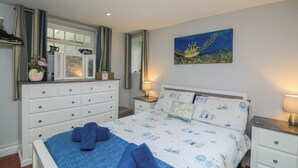 A bedroom with a bed, a dresser, a nightstand, a painting, and a window with curtains.
